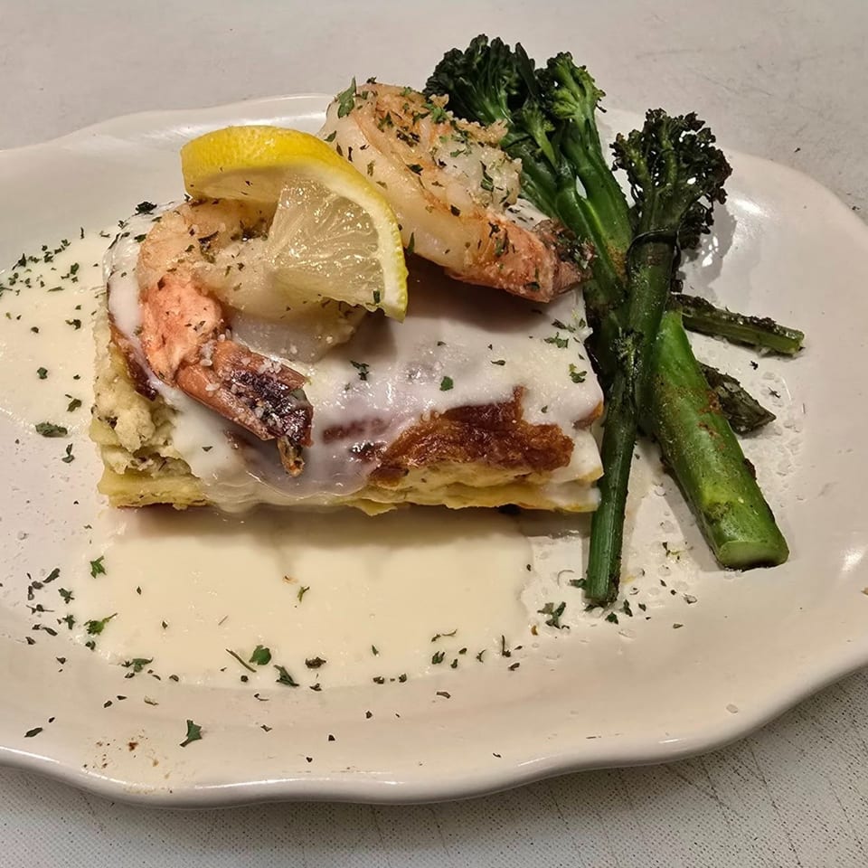 Gusto Dolce Italian Bistro's shrimp lasagna with creamy sauce, lemon, and broccolini on a white plate.