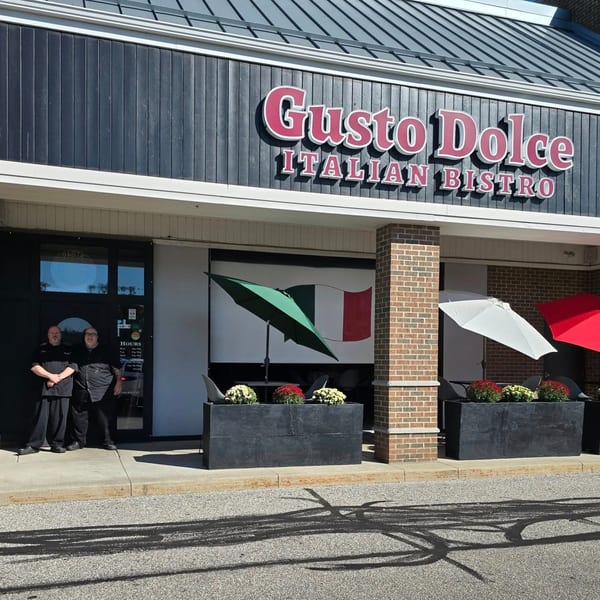 Exterior of Gusto Dolce Italian Bistro with two chefs, patio umbrellas, and an Italian flag.