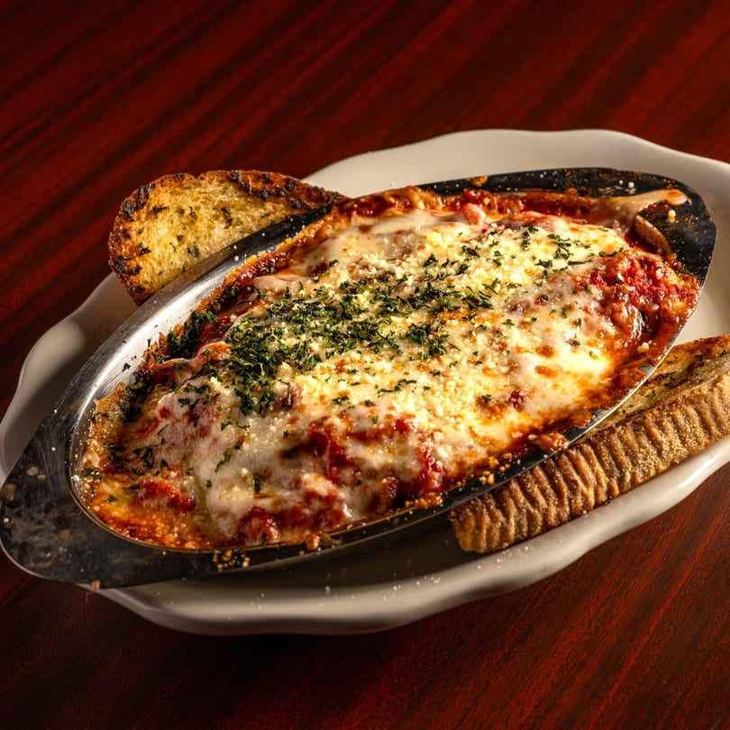 Baked Italian pasta dish with melted cheese and red sauce, garnished with parsley and garlic bread.