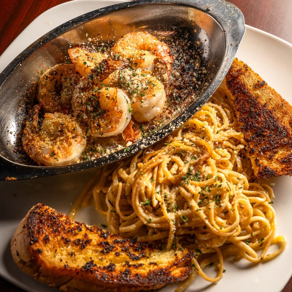 Shrimp scampi in a metal dish with linguine pasta and two pieces of garlic bread.
